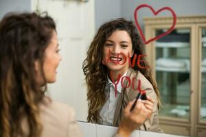 mujer de negocios es dibujo corazón y escritura yo amor usted con lápiz labial en el espejo mientras preparando para trabajo foto