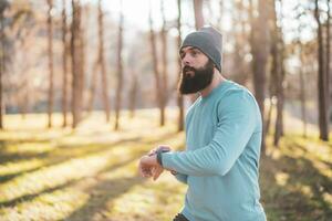 Sporty man looking at his watch during exercising in nature photo