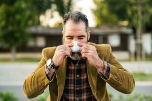 Modern businessman is blowing nose while sitting on the bench in the city photo