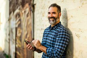 Businessman with a beard using mobile phone with digitized pen while standing in front of wall. photo