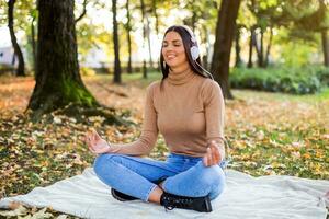 Beautiful woman meditating and listening music while resting and enjoys in autumn in the park photo