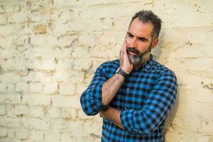 Deprimido empresario con barba en pie en frente de pared al aire libre foto
