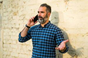 empresario con un barba teniendo conflicto mientras hablando con alguien en el teléfono foto