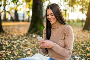 Beautiful woman texting messages while sitting in the park and enjoys in autumn photo