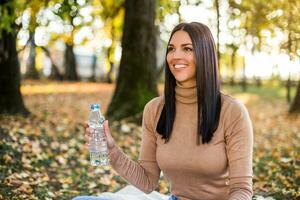 hermosa mujer Bebiendo agua mientras disfruta en otoño y descansando en el parque foto