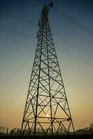 un silueta de un electricidad torre a puesta de sol foto