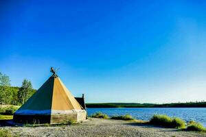 a teepee sits on the shore of a lake photo