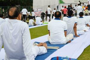 New Delhi, India, June 21, 2023 - Group Yoga exercise session for people at Yamuna Sports Complex in Delhi on International Yoga Day, Big group of adults attending yoga class in cricket stadium photo