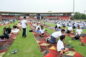 nuevo Delhi, India, junio 21, 2023 - grupo yoga ejercicio sesión para personas a yamuna Deportes complejo en Delhi en internacional yoga día, grande grupo de adultos asistiendo yoga clase en Grillo estadio foto