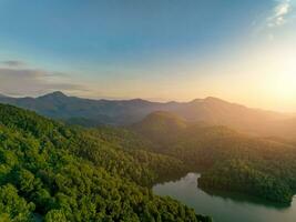 Beautiful landscape of green mountains and lake in the morning with sunrise sky. Nature landscape. Watershed forest. Water and forest sustainability concept. Aerial view of mountain with green trees. photo