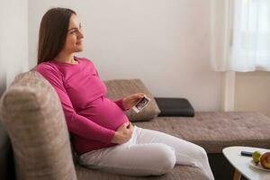 Pregnant woman sitting on the sofa and holding ultrasound picture. photo