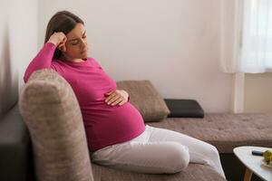Sad pregnant woman tired of pregnancy is sitting on sofa at her home. photo