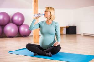 Pregnant woman drinking water in gym. photo