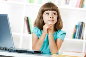 Little girl thinking while using laptop photo