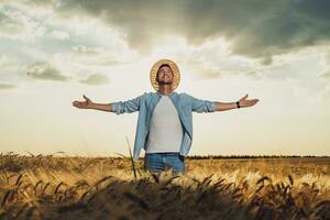 Happy farmer with arms outstretched standing in his growing barley field photo