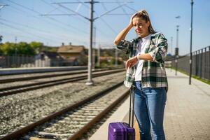 Upset woman looking at her clock while standing with suitcase on a train station. photo