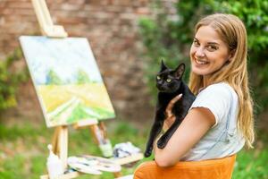 Woman enjoys spending time with her cat and painting on canvas outdoor photo