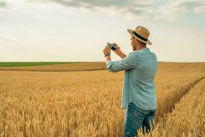 granjero utilizando móvil teléfono mientras en pie en su creciente trigo campo foto