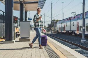 Woman with suitcase and ticket on a train station drinking coffee photo