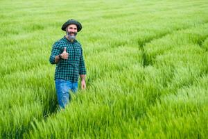 Happy farmer showing thumb up while standing in his growing wheat field photo