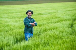 Happy farmer is standing in his growing wheat field photo