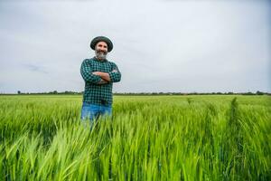 Happy farmer is standing in his growing wheat field photo