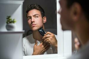 Man shaving  beard while looking himself in the mirror photo