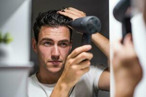 Man using hair dryer while looking himself in the mirror photo