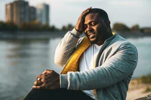 retrato de negro hombre teniendo un dolor de cabeza mientras sentado al aire libre foto