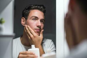 Man is applying aftershave while looking himself in the mirror photo