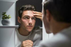 Man looking at his wrinkles while standing in front of mirror photo