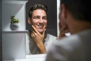 retrato de hombre mirando él mismo en un espejo mientras en pie en baño foto