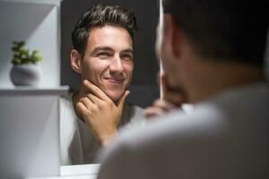 retrato de hombre mirando él mismo en un espejo mientras en pie en baño foto