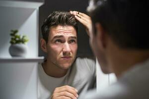 Worried man is looking his hair in the mirror photo