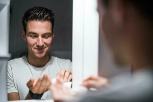 Man is applying aftershave while standing in front of mirror photo