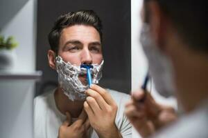 Man shaving  beard while looking himself in the mirror photo