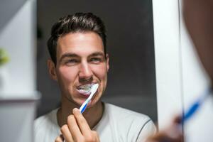 Man is brushing teeth while looking himself in the mirror photo