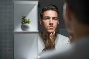 retrato de hombre mirando él mismo en un espejo mientras en pie en baño foto