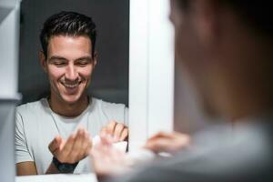 Man is applying aftershave while standing in front of mirror photo