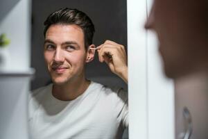 Man cleaning ear while looking himself in the mirror photo