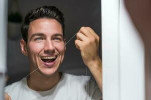 hombre es utilizando dental seda floja mientras mirando él mismo en el espejo foto