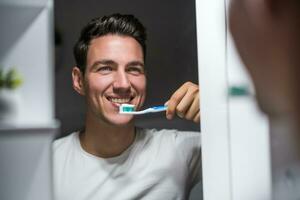 Man is brushing teeth while looking himself in the mirror photo