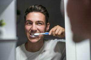 hombre es cepillado dientes mientras mirando él mismo en el espejo foto