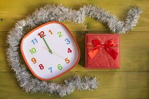 Image of decorated clock showing midnight and gift in beautiful red box on wooden table photo