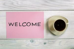 Welcome sign on pink paper with cup of coffee on wooden table photo