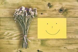 Beautiful bouquet of flowers and smiley face on wooden table photo