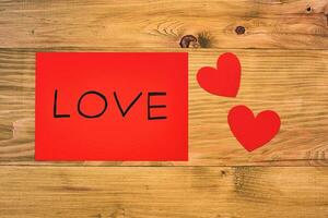 Red paper with word love and heart shapes on wooden table photo
