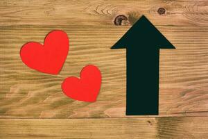 Photo of two red hearts and arrow on wooden table, love growth concept