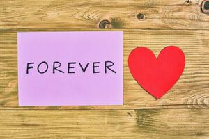 Forever word on paper with heart on wooden background photo