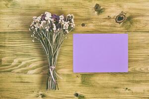 Beautiful bouquet of flowers and empty paper for text on wooden table photo